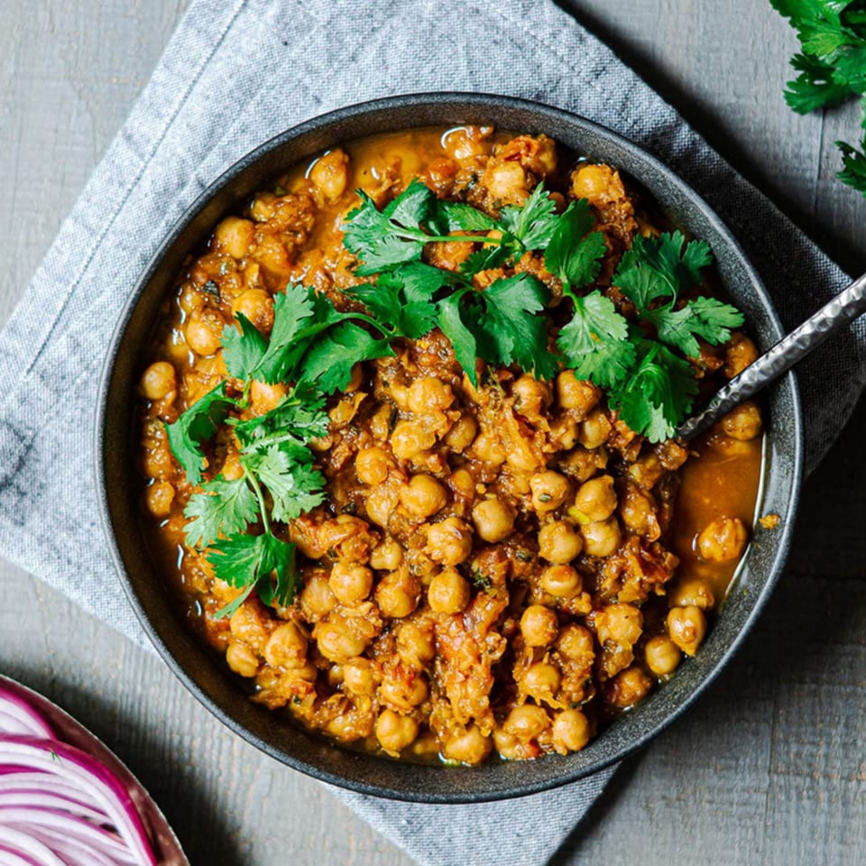 A black bowl of Indian chana masala, garnished with fresh cilantro, on a wooden table.