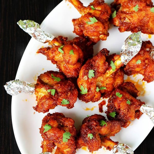 A white plate filled with India Clay Oven's chicken lollipops, garnished with fresh cilantro.