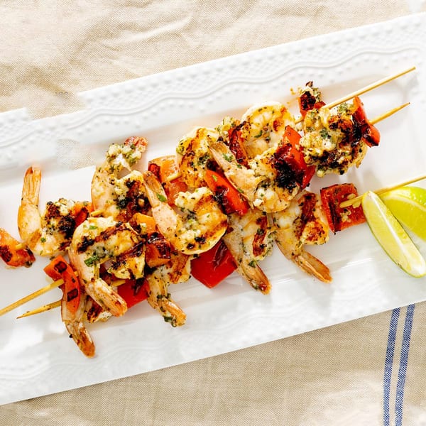 Grilled shrimp and red bell pepper skewers with lime wedges on a white plate.