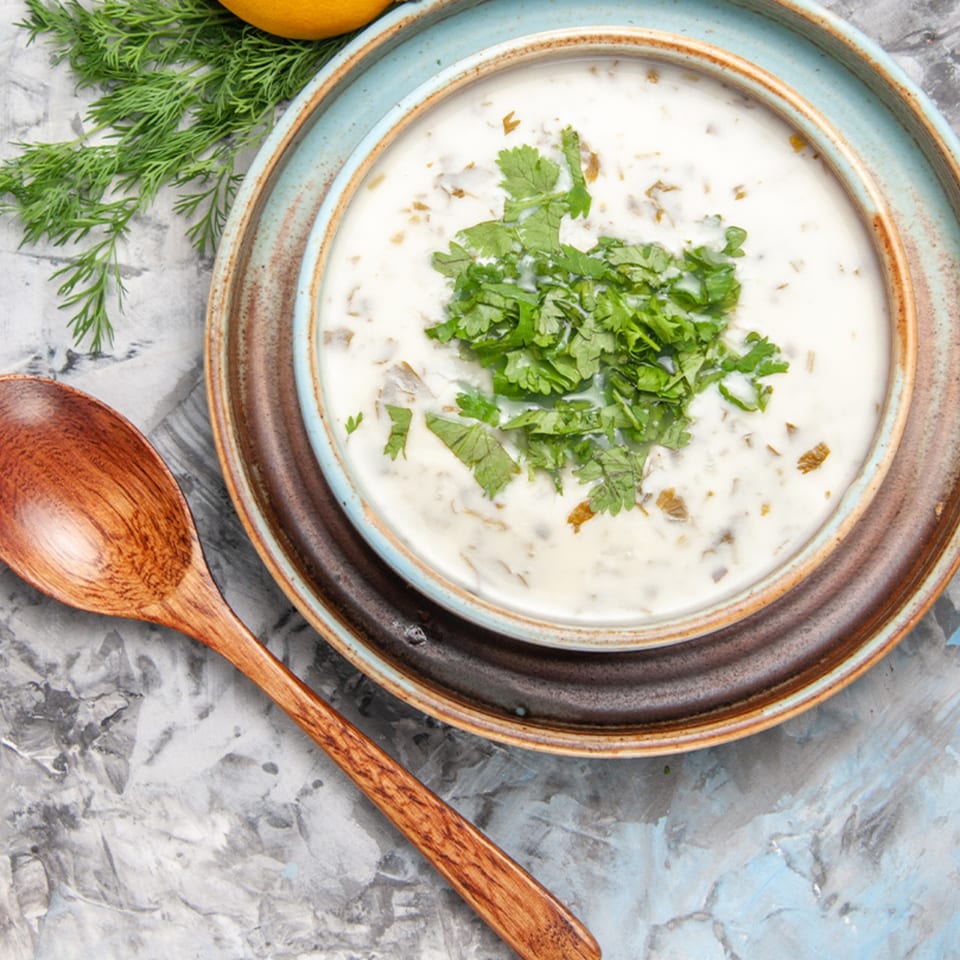 Overhead view of a bowl of Indian raita, garnished with fresh cilantro, next to a wooden spoon.
