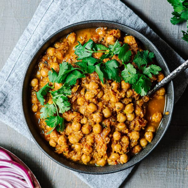 A black bowl of Indian chana masala, garnished with fresh cilantro, on a wooden table.